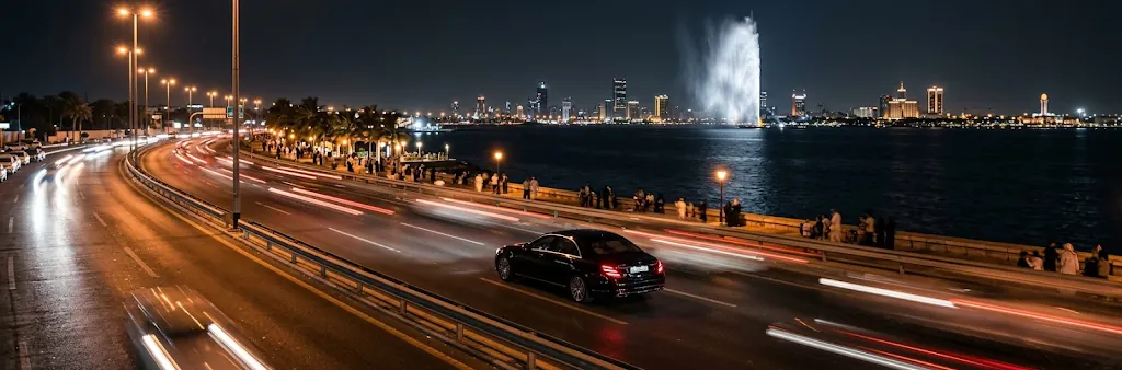 Black sedan driving along the Jeddah Corniche at night with King Fahd's Fountain